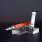 Pen with red and silver design on a clear stand against a dark background