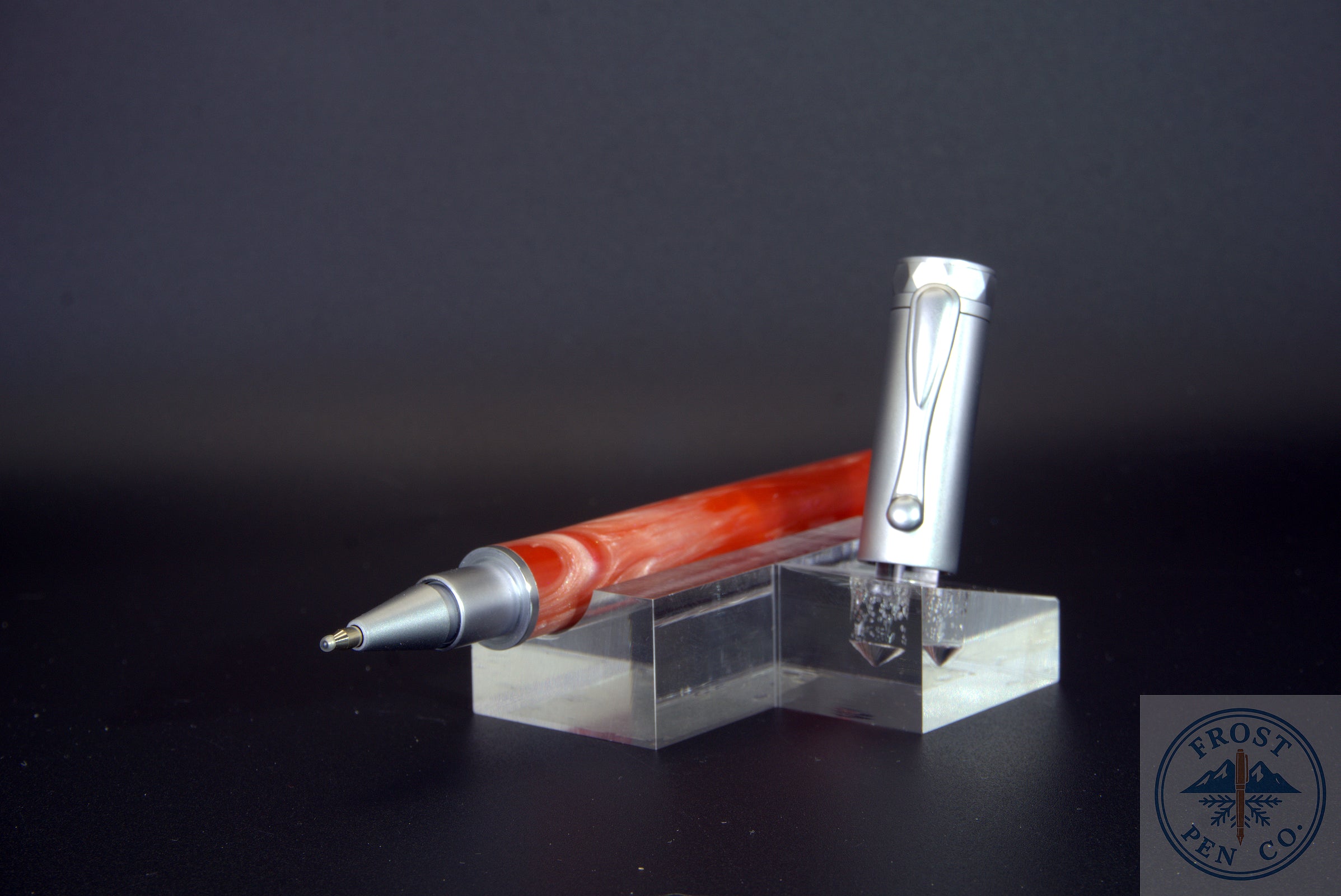 Pen with red and silver design on a clear stand against a dark background