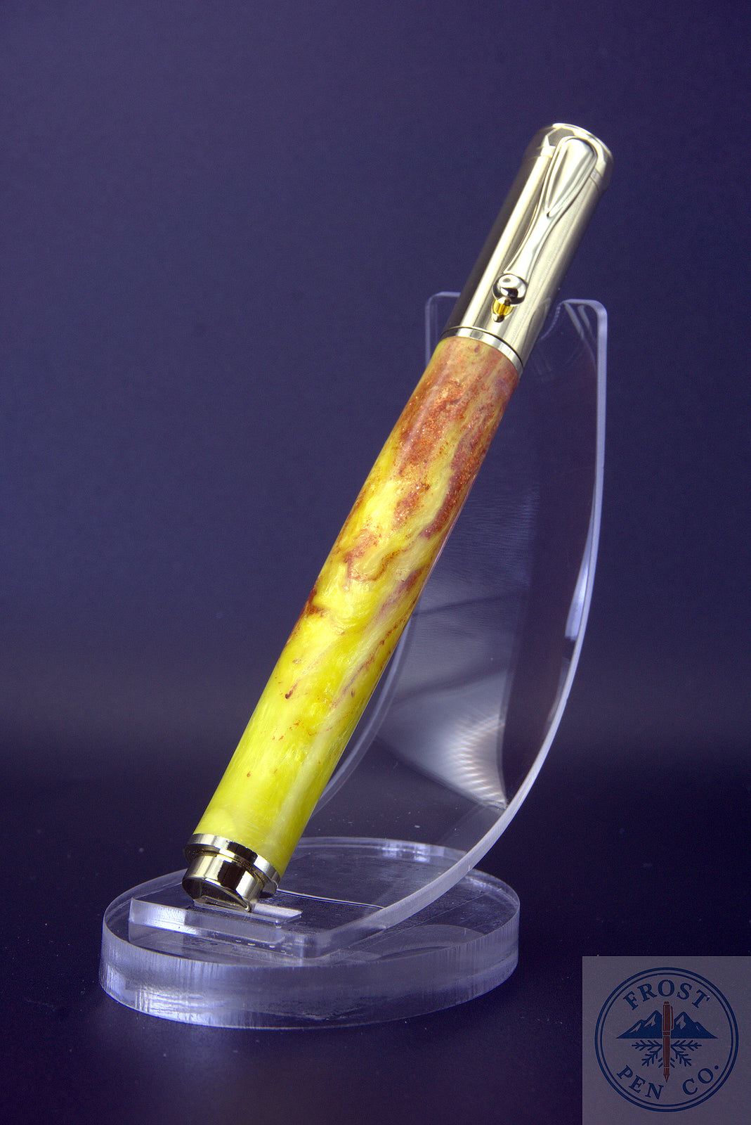 Fountain pen with yellow and brown body on a clear stand against a dark background