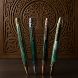 Four green pens with gold accents on a wooden surface with intricate carvings.